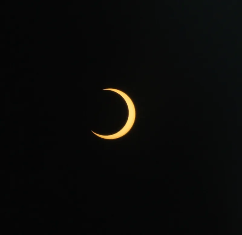 An annular solar eclipse shows the dark shape of the moon in front of the orange sun.