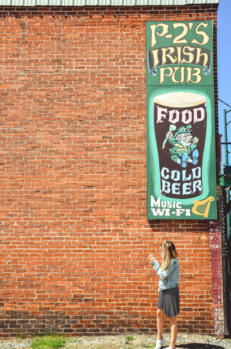The signage for P-2's Irish Pub is seen against a brick wall with an individual standing beneath it.