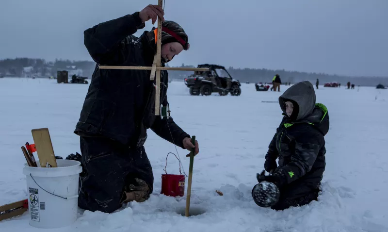 A man and small boy prepare a hole in the ice to go fishing.