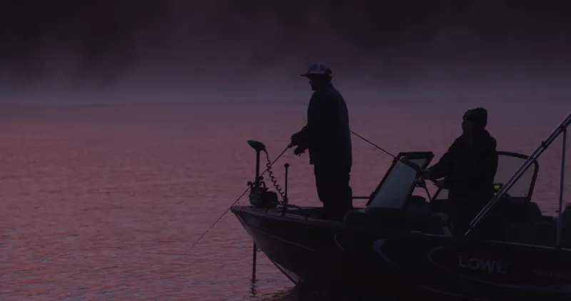 The lake water glows pink in the early morning sun as a man and a woman fish from a boat