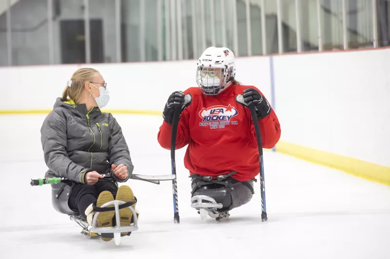 Two women talking on sled hockey sleds on the ice