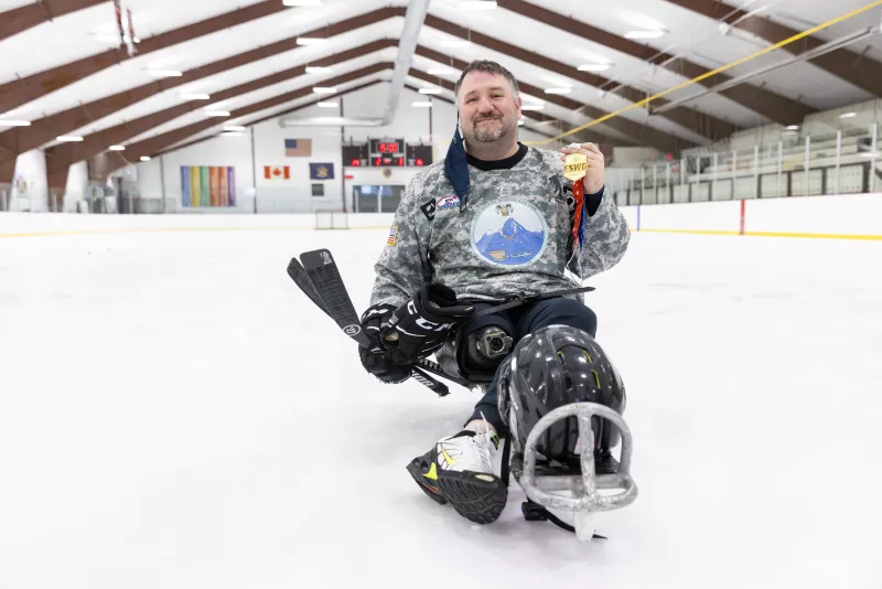Smiling man on sled hockey sled with medal
