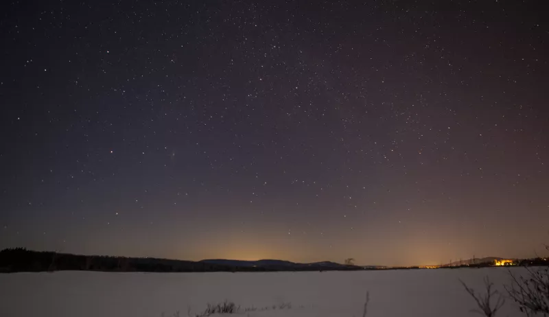A view of the starry night sky over snowy, frozen Tupper Lake.