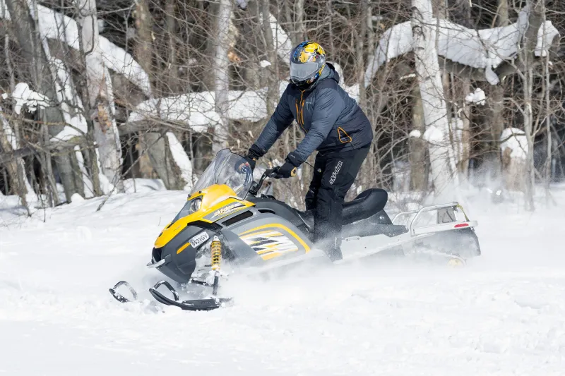 A person in a black snowsuit on a yellow snowmobile rides in fresh powder.