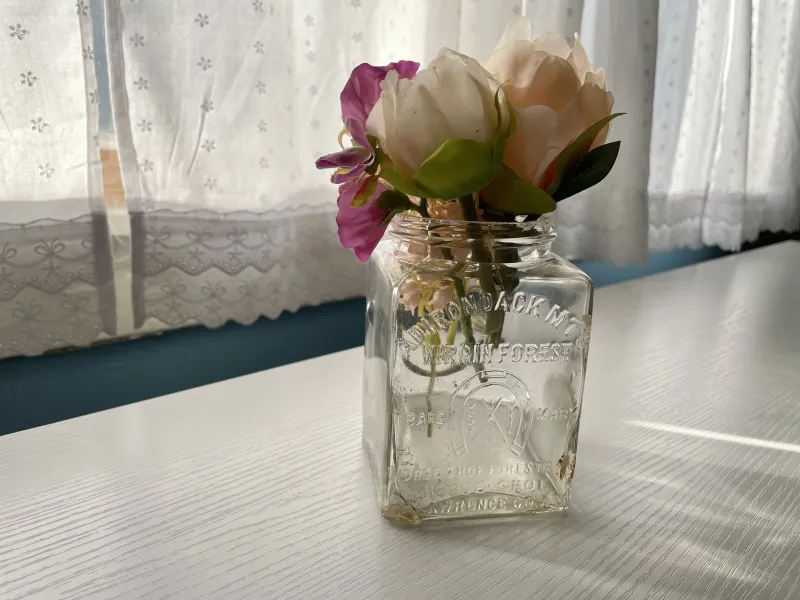 An antique square glass bottle with artificial flowers in it.