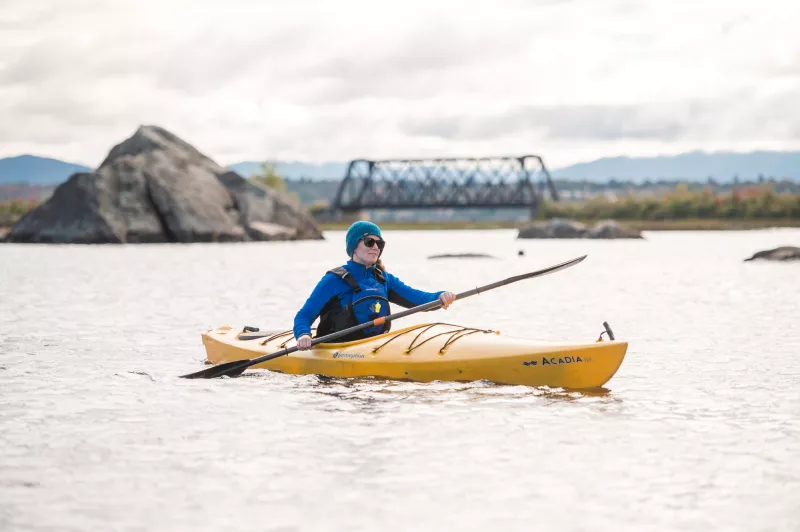 A paddler in a kayak in front of a bridge and large rocks.