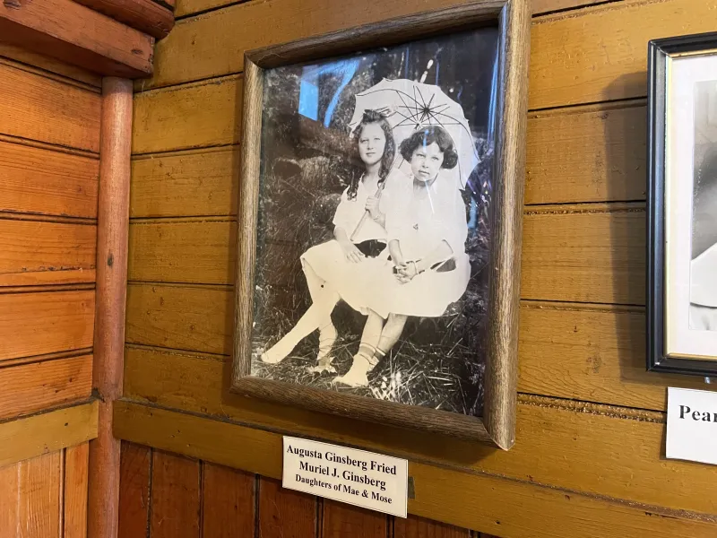 A vintage black and white photo of two girls in dresses hangs in a frame on a wood-paneled wall.