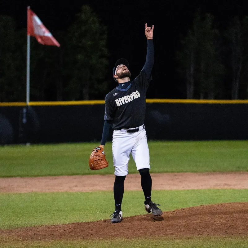 A baseball pitcher stands on the mound and points toward the sky.