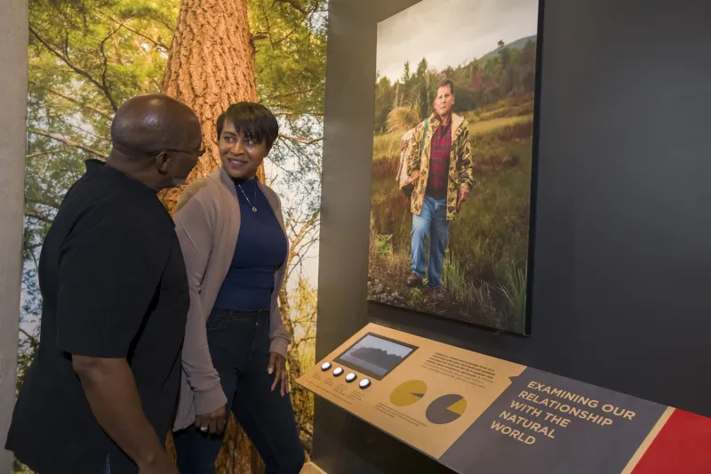 A man and a woman exchange a smile as they view an interactive display at the Climate Solutions exhibition at The Wild Center.