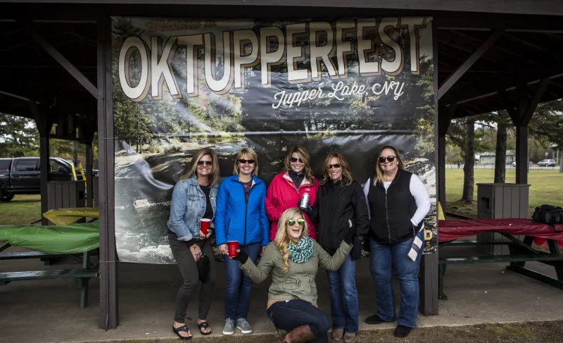 a group of women in fall clothing pose in front of an okTupperfest.