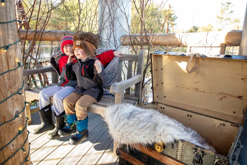 Two young boys sit outside at The Wild Center during winter.