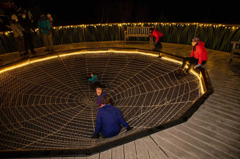 A family sits in the giant spider web on The Wild Walk at The Wild Center