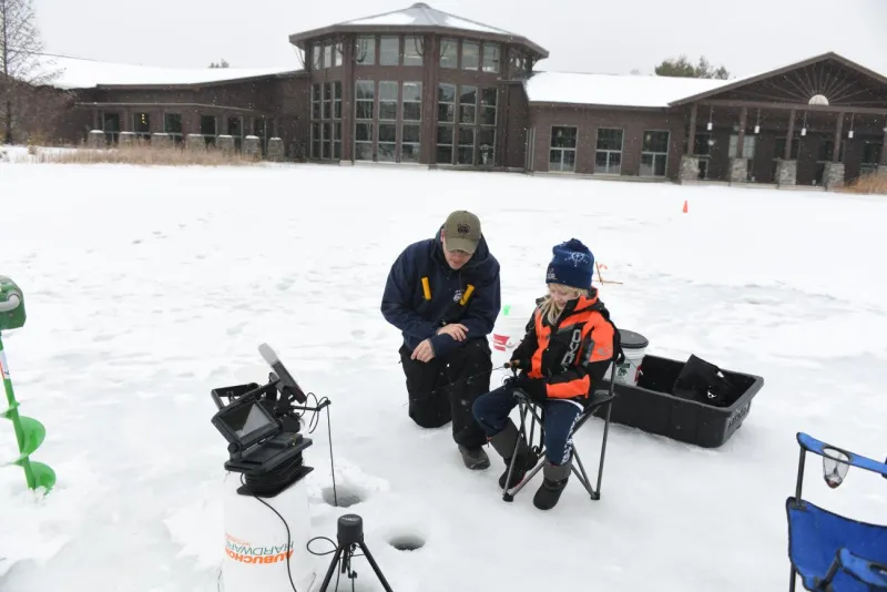 A child learns to ice fish with staff at the Wild Center on a frozen pond