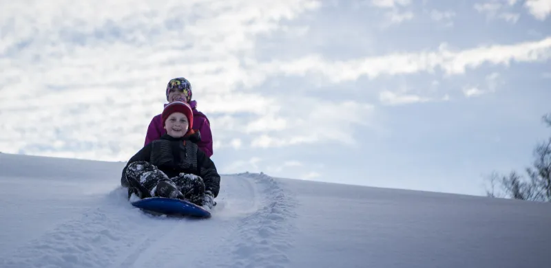 Two kids grin wildly as they sled down a snowy hill