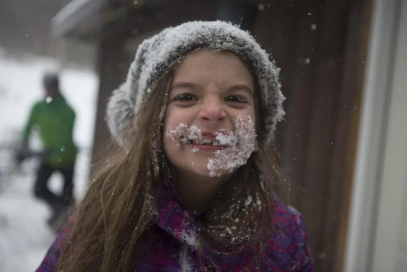 A young girl smiles from ear to ear with snow on her face