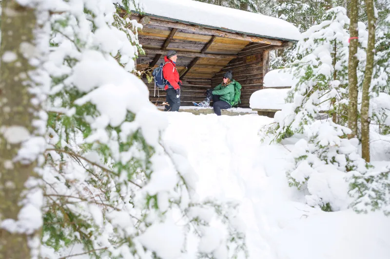 Two people relax in a lean to in winter as they take a break from snowshoeing