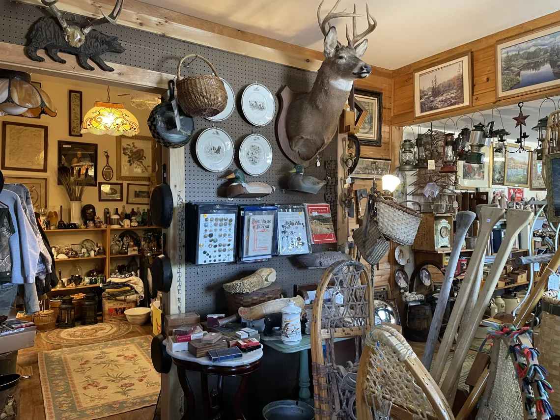 An antique shop is crowded with items on shelves and walls, many with a rustic Adirondack theme.