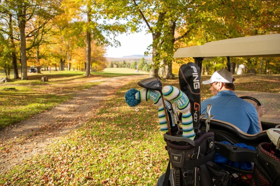 A golfer drives a cart among brightly colored trees of fall foliage while golfing in Tupper Lake.