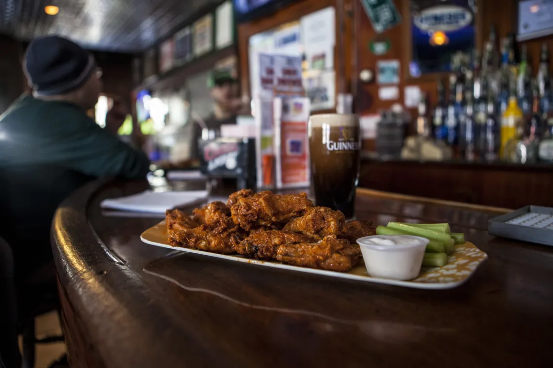 A full pint of Guinness rests behind a platter of fried chicken wings and a side of celery sits on the bar at P-2's Irish Pub