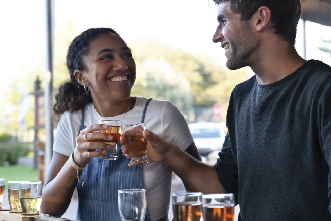 A couple smiles at each other while sharing a flight of drinks at Raquette River Brewing's outdoor seating area in Tupper Lake