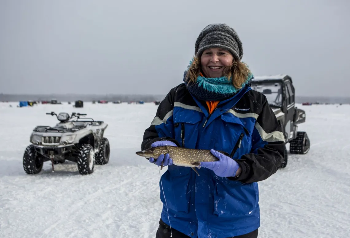 A woman shows off her most recent ice fishing catch in Tupper Lake, New York