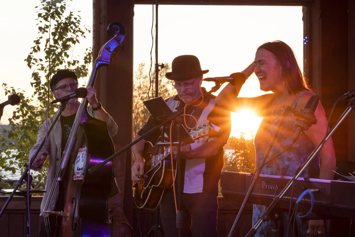 A 3-person band performs outdoors at sunset