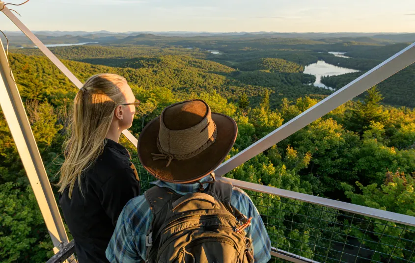 Two people look at the view from a spot on the stairs up a firetower