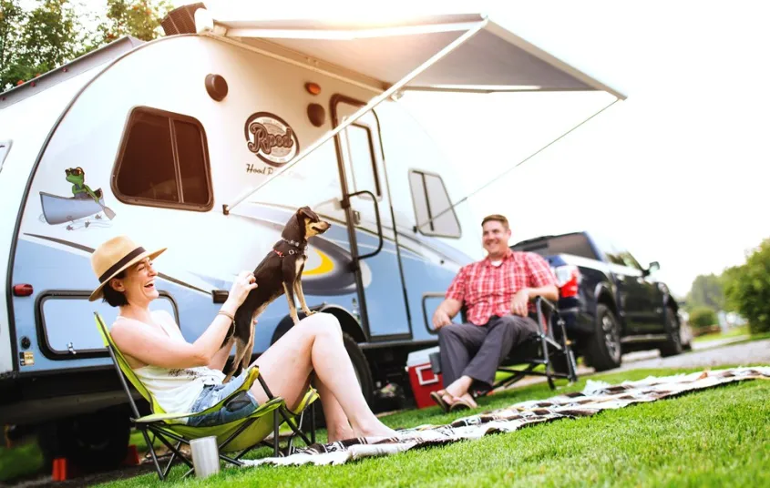 People smile and laugh in lawn chairs under the awning of their camper