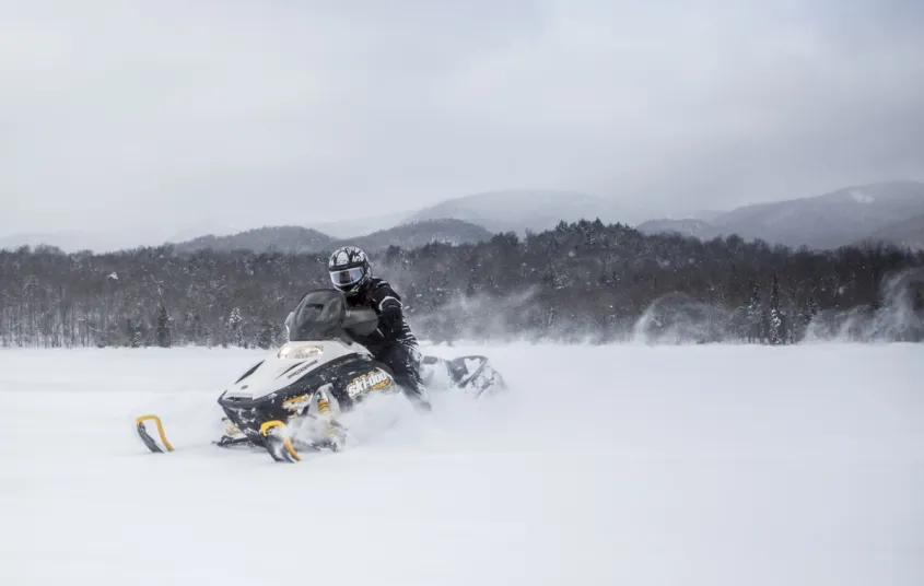A person on a black and yellow snow machine in a field.