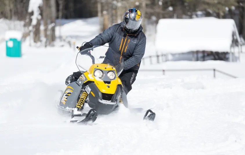 A person on a black and yellow snow machine rips through the snow.