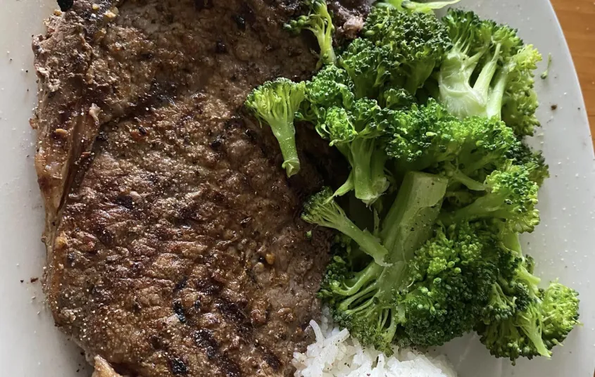 A huge steak with perfect grill crosshatches with rice and broccoli.