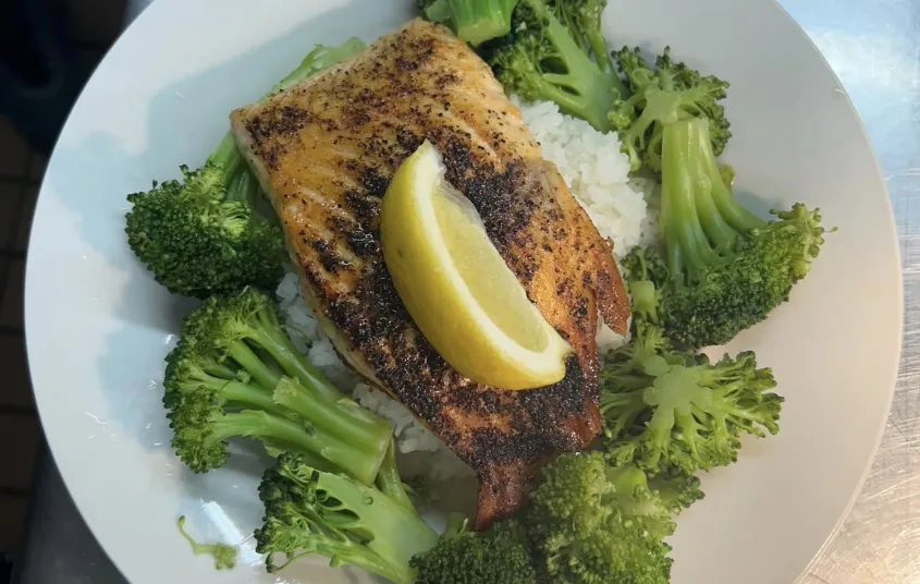 Salmon over rice with broccoli and a lemon wedge on a white plate.