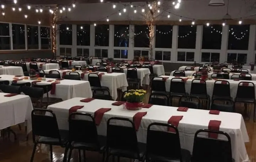 An event space set with white linen and rust accent napkins and lit with Edison string lights.