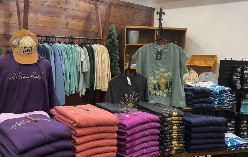 Stacks of colorful folded shirts with racks of hanging closthes.