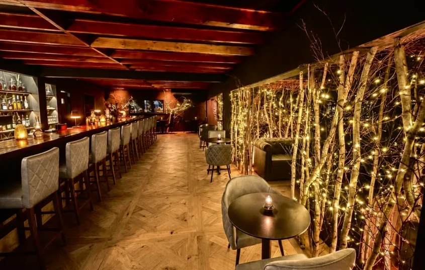 Leather chairs and warm wood at the bistro tables and couches as booths between white birch and twinkle lights.