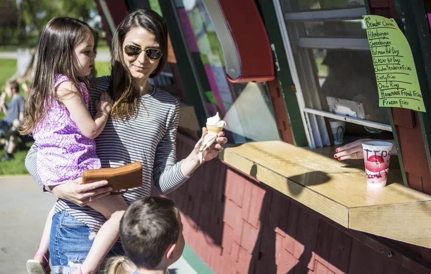 A mom holds her kid in one hand and an ice cream cone in the other.