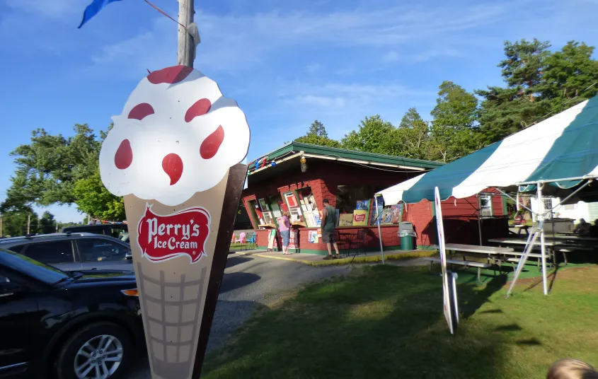 Kids sit on the arm of a giant red adirondack chair while enjoying ice cream cones.