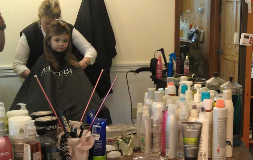 A little girl sits in the cutting chair.