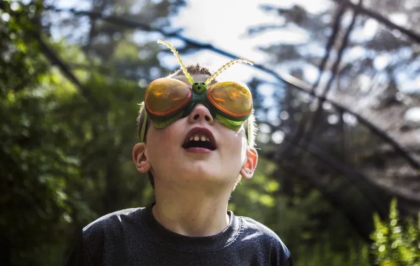Kid wears bug glasses in the butterfly house at Paul Smiths VIC