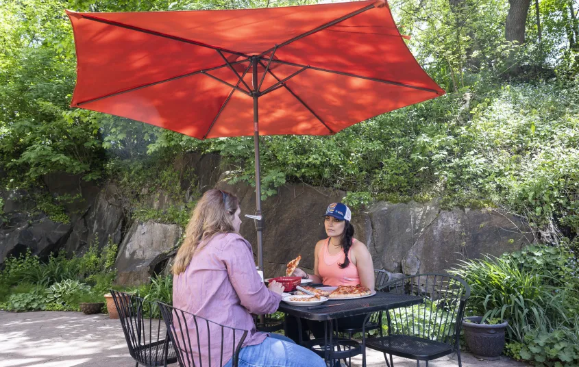 Two ladies have a meal at a metal bistro set with red umbrella