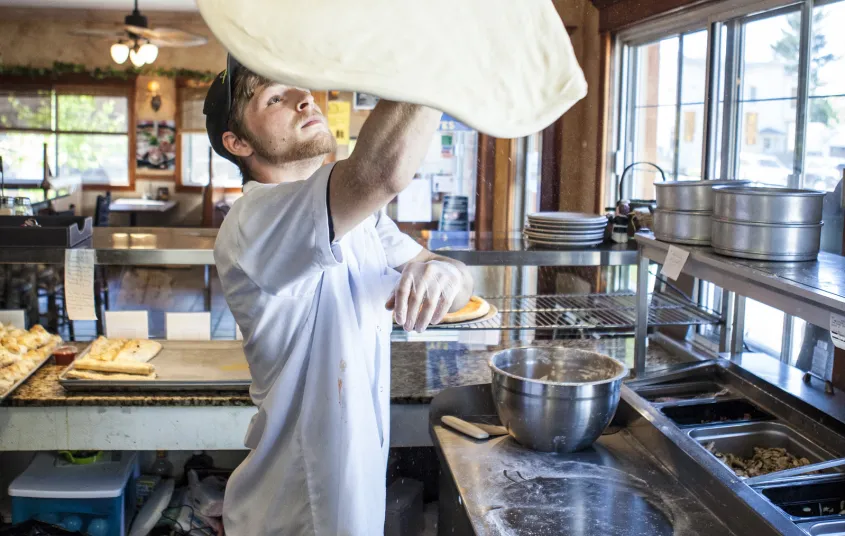 Pizza dough is being tossed above a man's head.