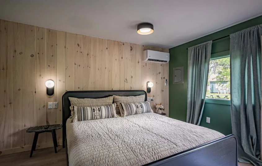 A large cream colored bed with brown striped pillows and pine walls.