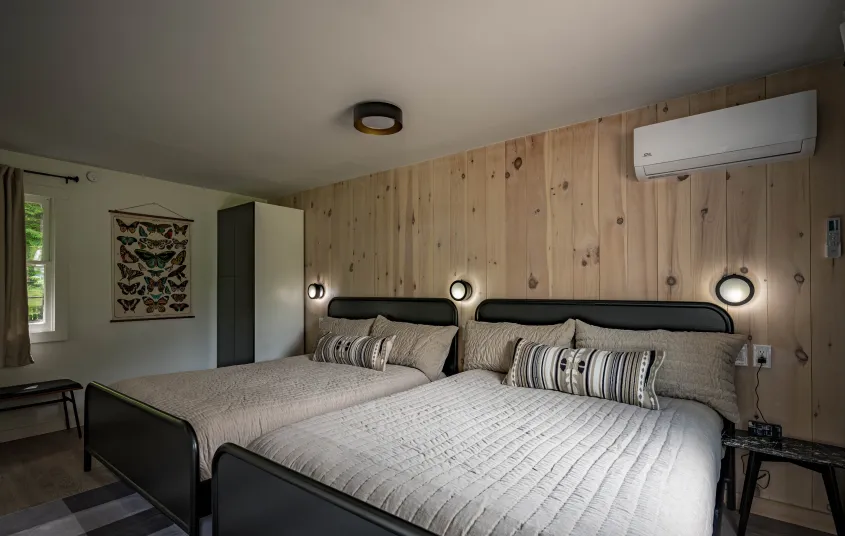 A two queen room with knotty pine paneled walls behind the dark headboard.