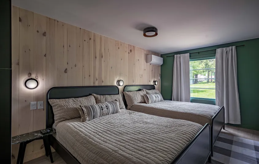 A two queen room with knotty pine paneled walls behind the dark headboard.