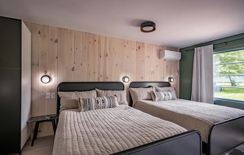 A two queen room with knotty pine paneled walls behind the dark headboard.