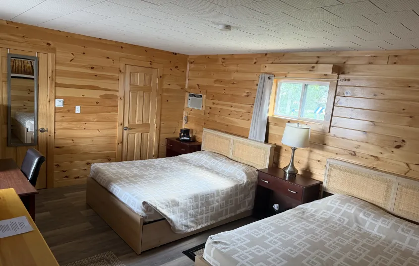 Two queen sized beds in a room with walls covered in knotty pine paneling at the Tupper Lake Motel.