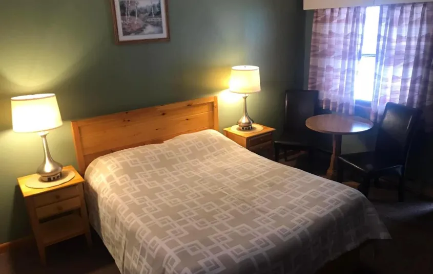 A king sized bed in a room with pine green walls at the Tupper Lake Motel.