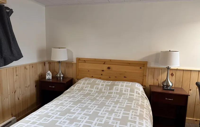 The king bed in a room with knotty pine wainscoting at the Tupper Lake Motel.
