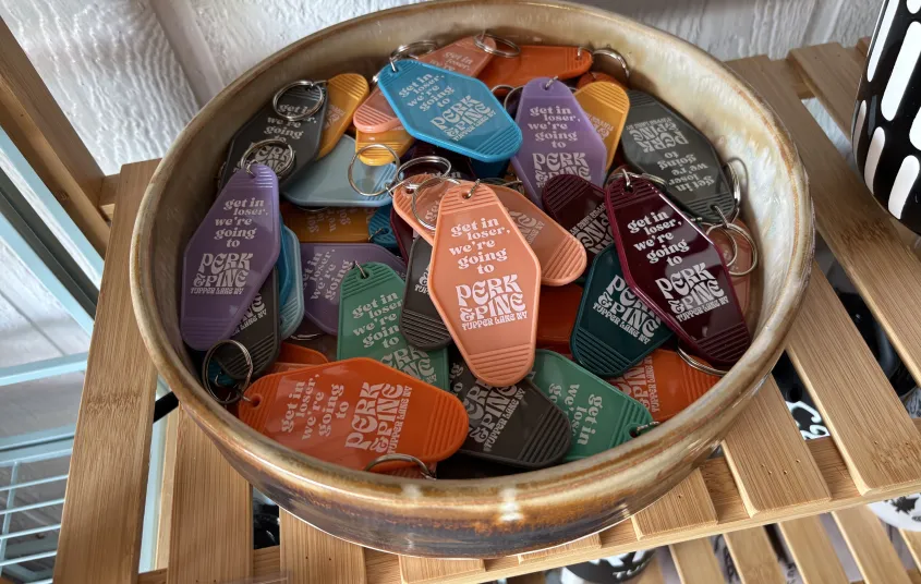 A takeaway paper cup with custom Perk and Pine cardboard sleeve on a wooden window sill next to a plant potted in a disco ball