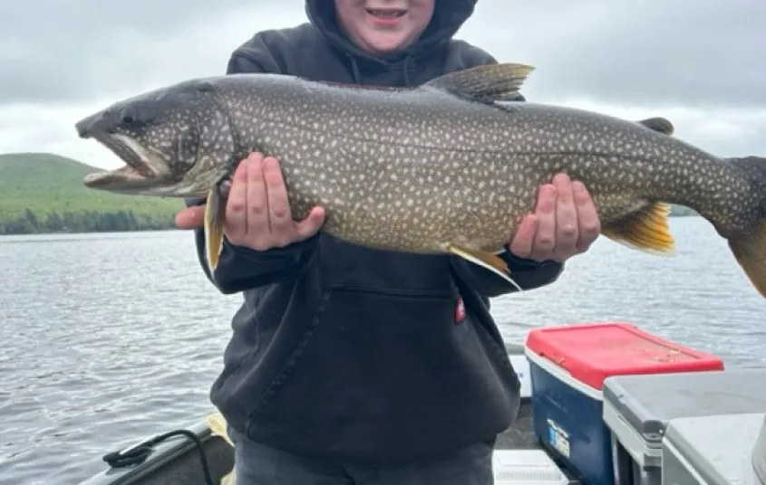 A smiling kid standing on a boat holding a large fish.